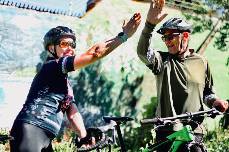 Alison Blair and Craig Vandeleur giving each other a high five with their bicycles